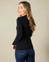 Woman wearing a black long-sleeve top and blue jeans against a beige background