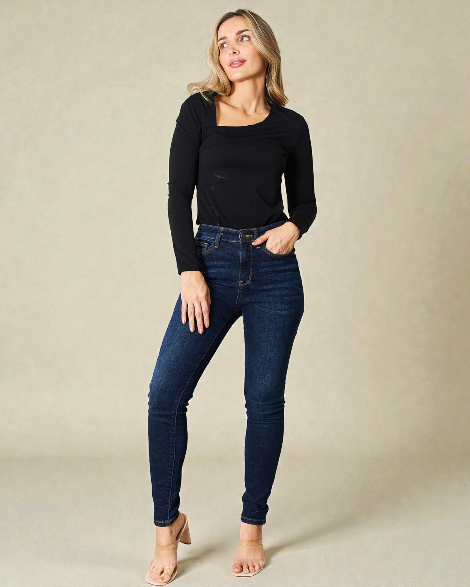 Woman wearing dark blue jeans and a black top against a beige background