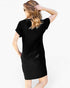 A woman shown from the back wearing a plain black short-sleeve mini dress against a light gray studio background.