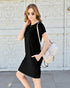 Woman wearing a black dress with sunglasses and a backpack against a textured wall.