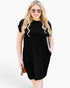 A woman modeling a black short-sleeve shift dress with side pockets, styled with sunglasses and holding a small brown clutch against a plain white studio background.