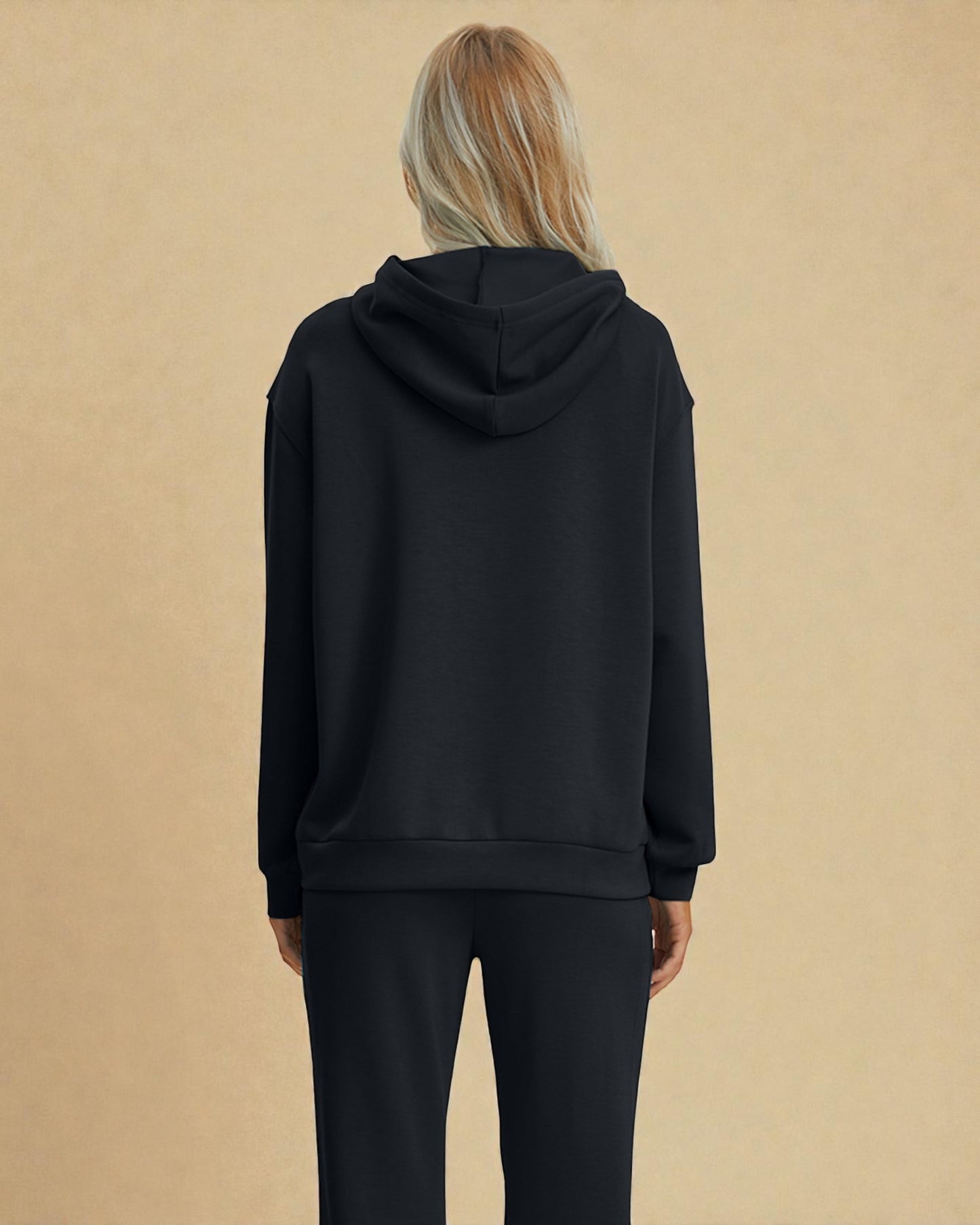 Person wearing a black hoodie and pants on a beige background