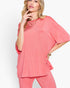 A woman modeling a coral pink short-sleeve tunic top with matching pink pants against a clean white studio background.