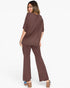 A woman modeling a matching two-piece lounge set in a solid brown color, featuring an oversized short-sleeve top and wide-leg pants, shown from a rear three-quarter angle against a plain white background.