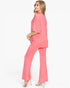 A woman modeling a two-piece pink lounge set consisting of a short-sleeve top and matching wide-leg pants, shown from a side-back angle against a plain white studio background.