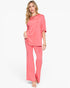 A woman modeling a coral pink two-piece lounge set consisting of a short-sleeve top and matching wide-leg pants, photographed against a solid white studio background.