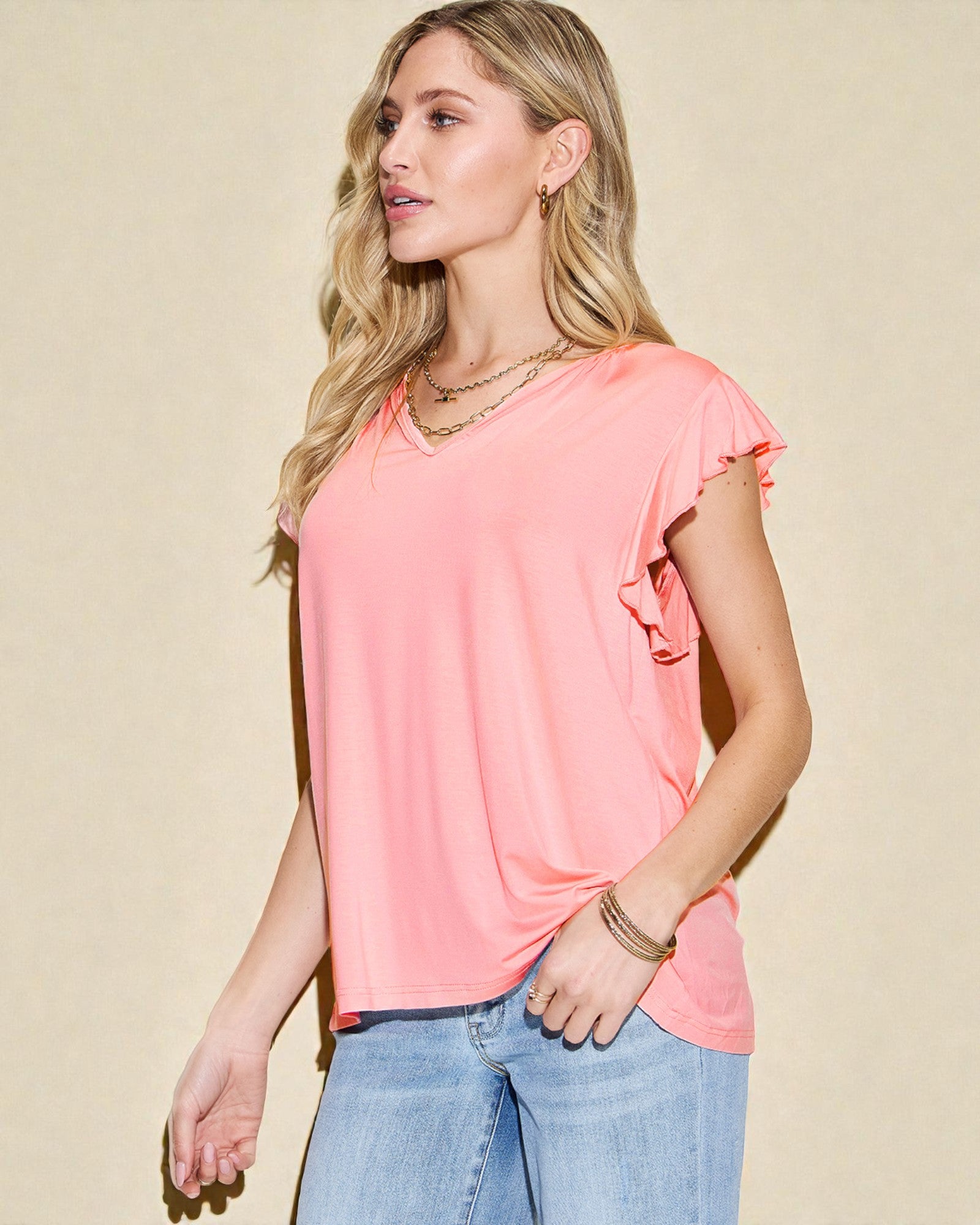 Woman wearing a coral ruffled top and blue jeans against a beige background