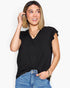 A woman wearing a black short-sleeve top with ruffled edges and a twisted front detail, paired with blue jeans, against a plain light gray background.