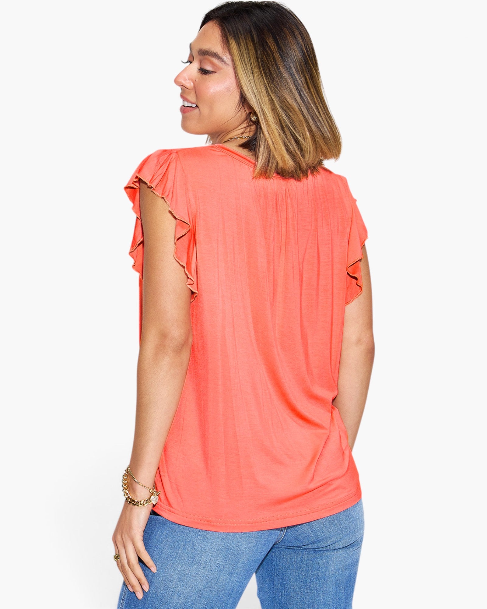 A woman shown from the back wearing a coral orange short-sleeve top with ruffled shoulder details and blue jeans, against a plain white background.
