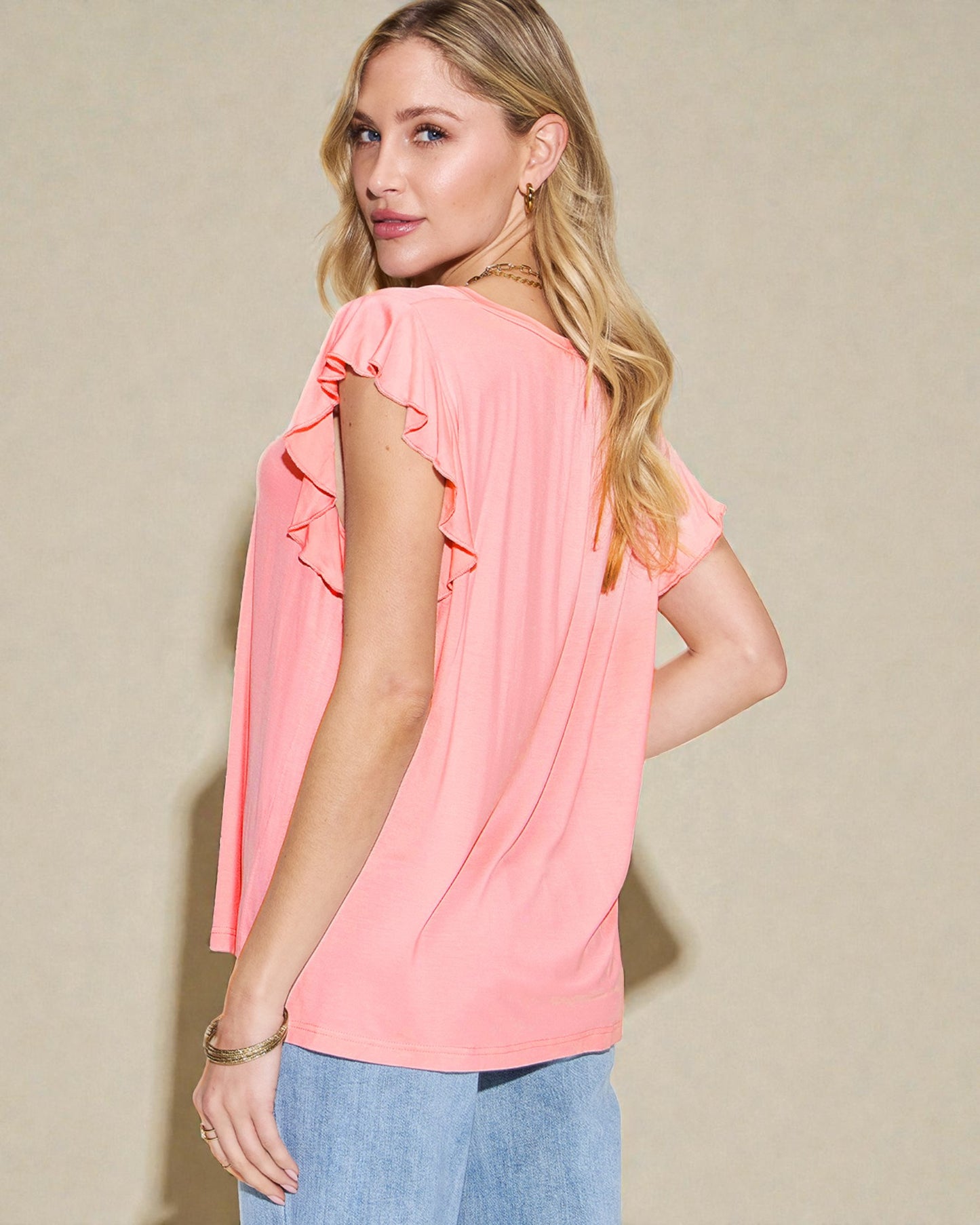 Woman wearing a pink blouse with ruffled sleeves against a beige background