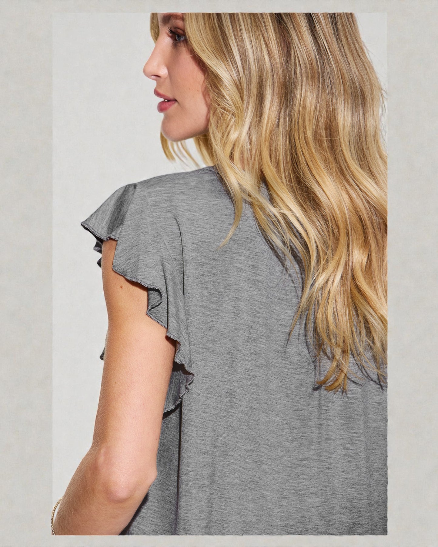 Woman wearing a gray ruffled sleeve top with a plain background