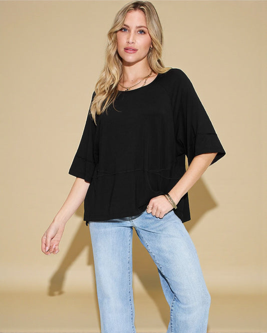 Woman wearing a black top and light blue jeans against a beige background