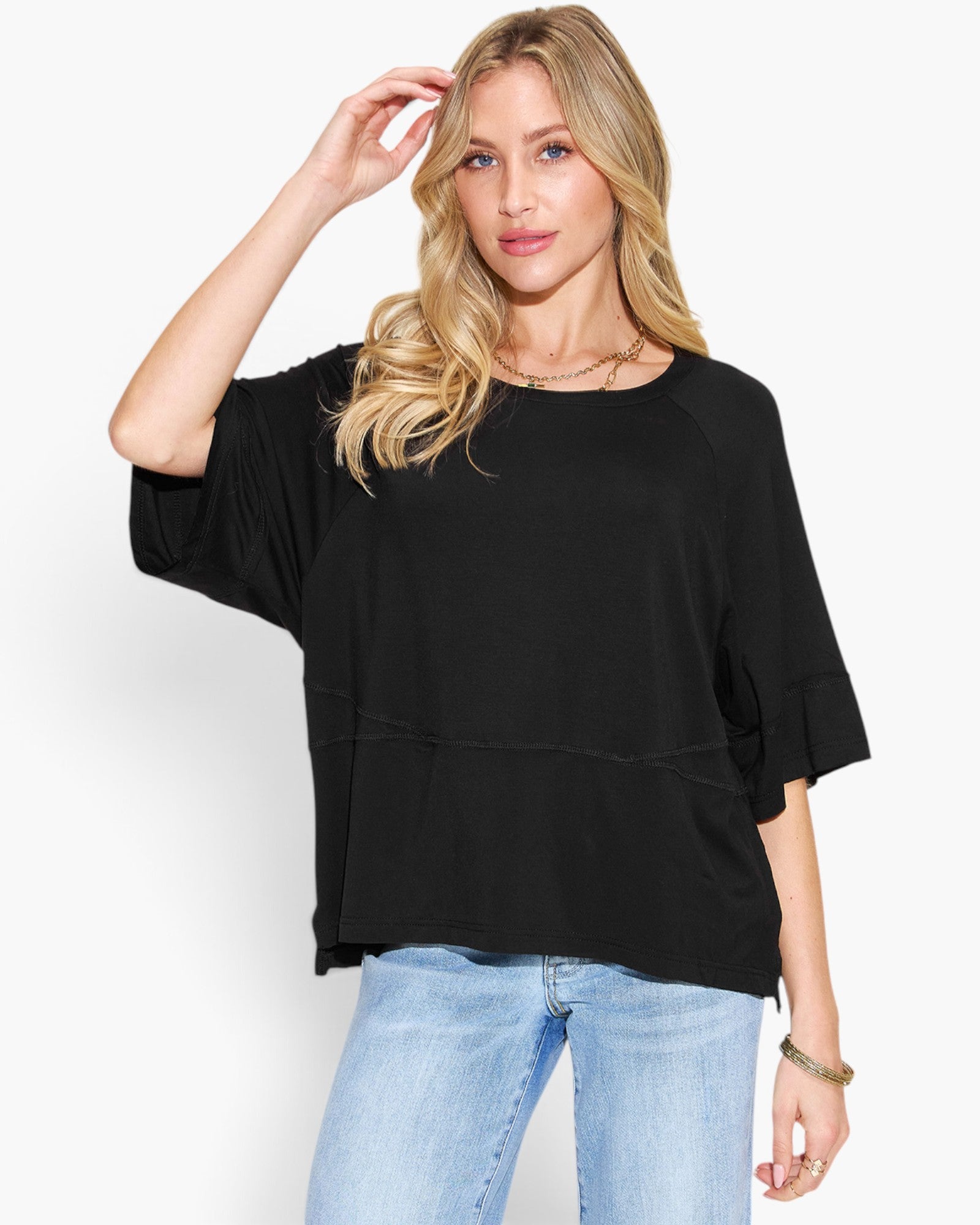A woman modeling a black short-sleeve top with a relaxed, slightly oversized fit and light blue jeans against a plain white studio background.