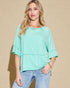 Woman wearing a light green top and blue jeans against a beige background