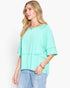 A woman wearing a mint green tiered short-sleeve top and light blue jeans, photographed against a clean white studio background.