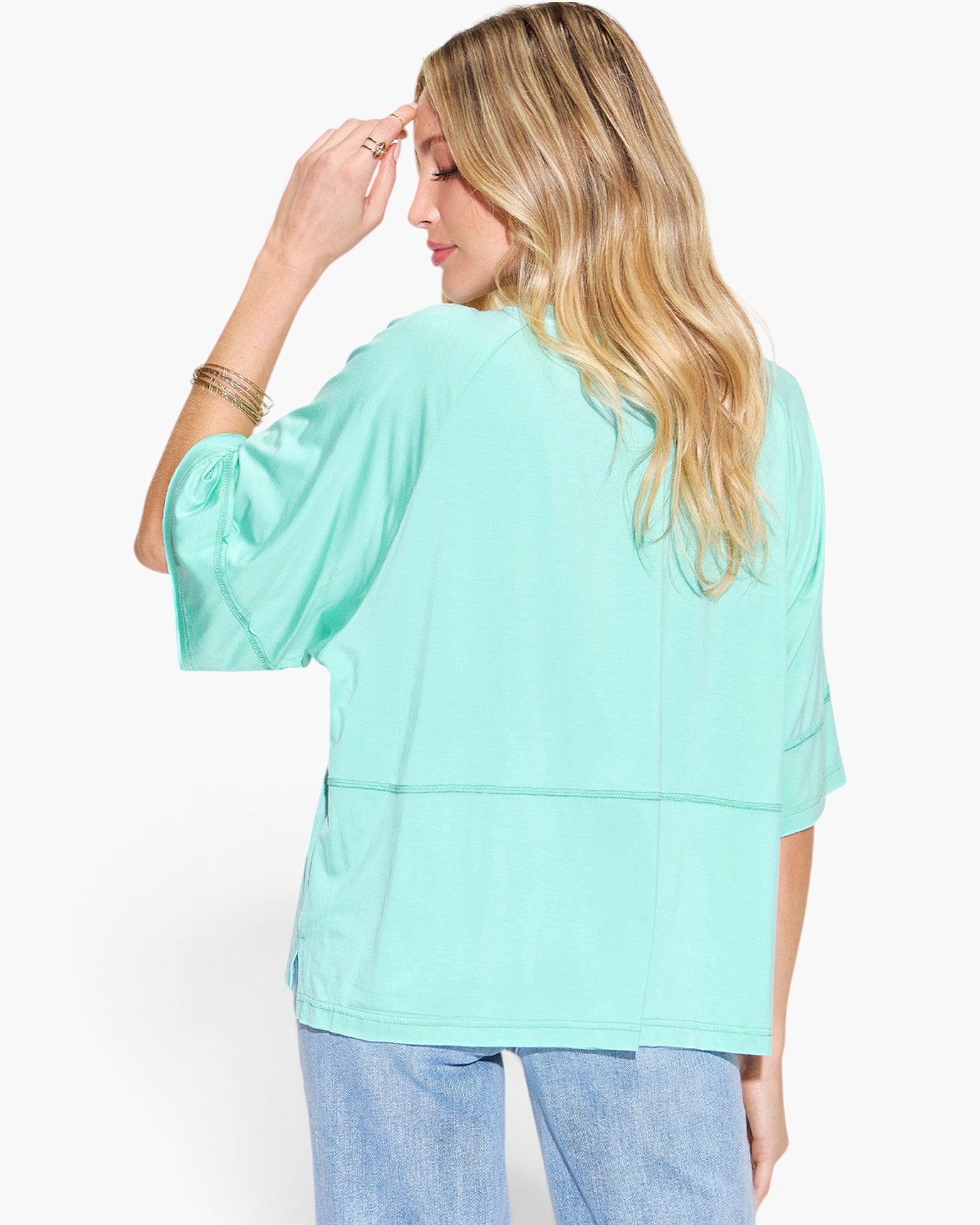 A woman shown from the back wearing a mint green short-sleeve top and light blue jeans against a plain white background.