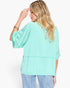 A woman shown from the back wearing a mint green short-sleeve top and light blue jeans against a plain white background.