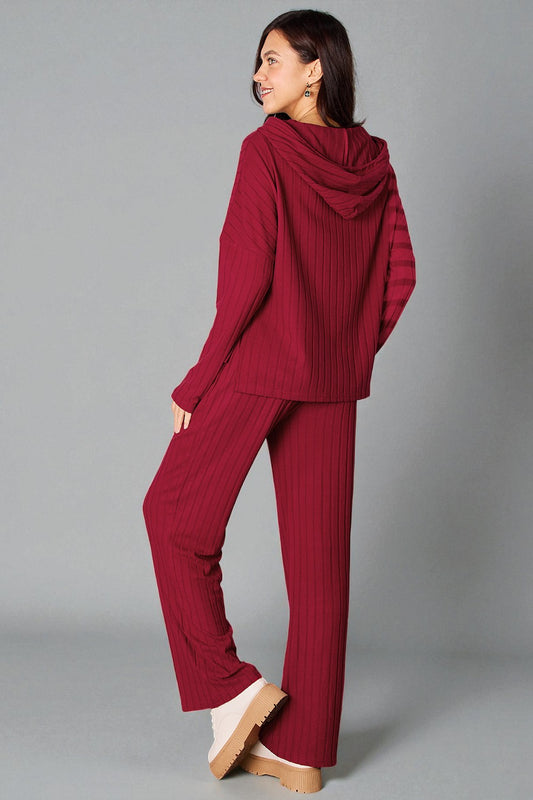 Woman wearing a red ribbed sweater and pants on a gray background