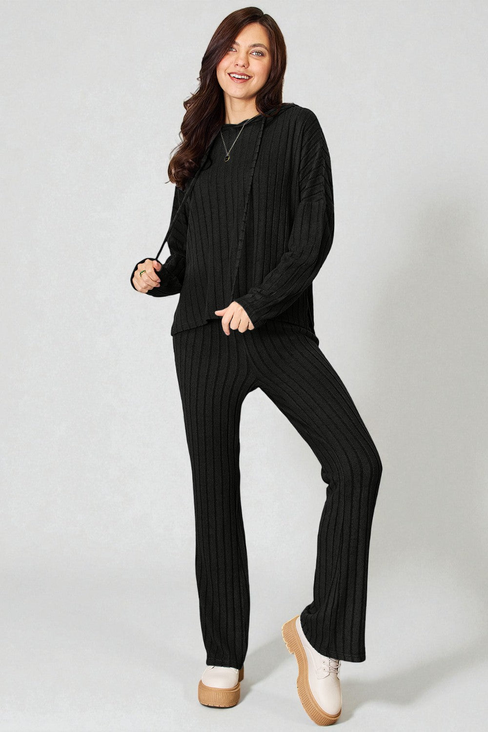 Woman wearing a black ribbed sweater and pants on a white background