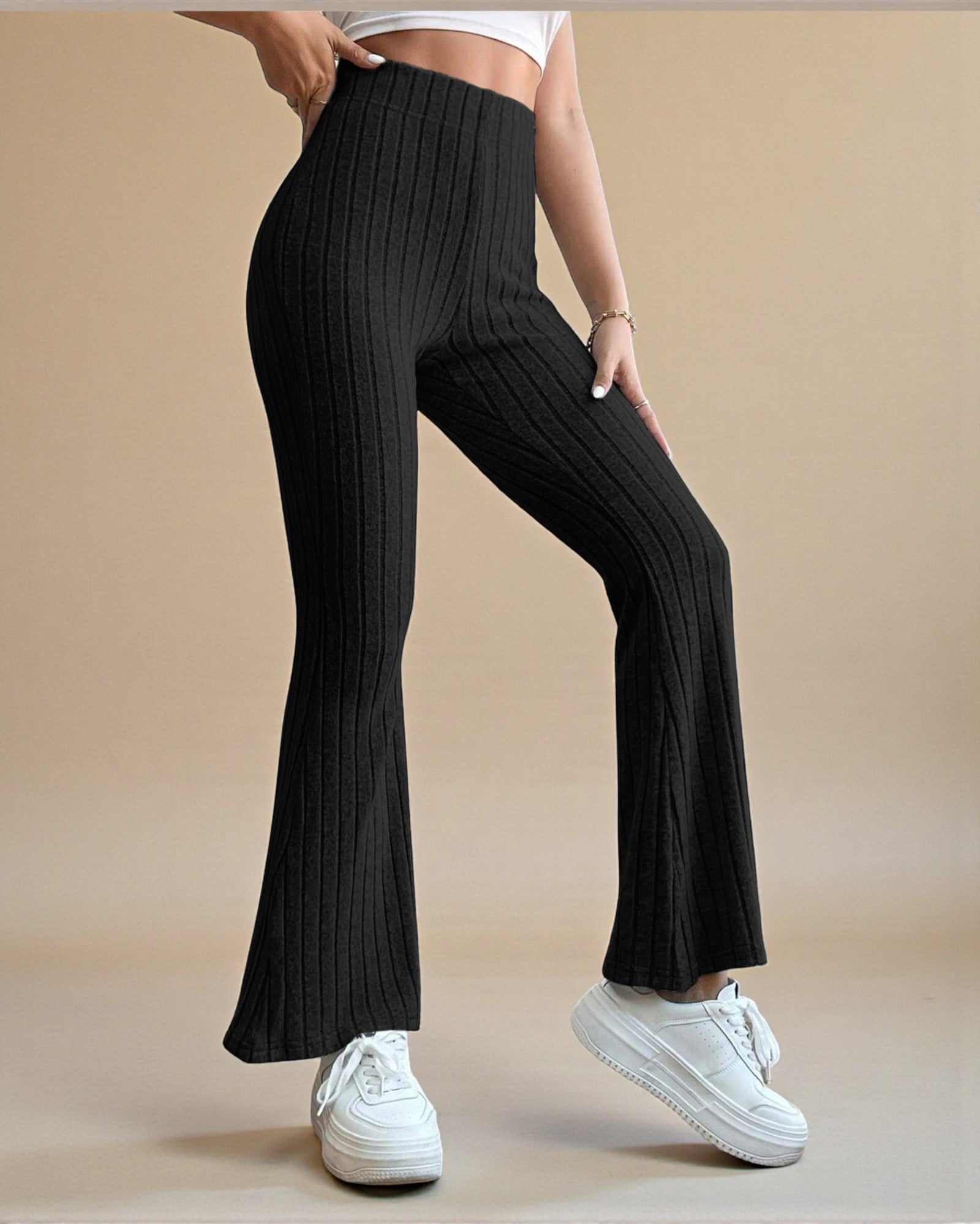 Person wearing black ribbed flared pants and white sneakers on a beige background