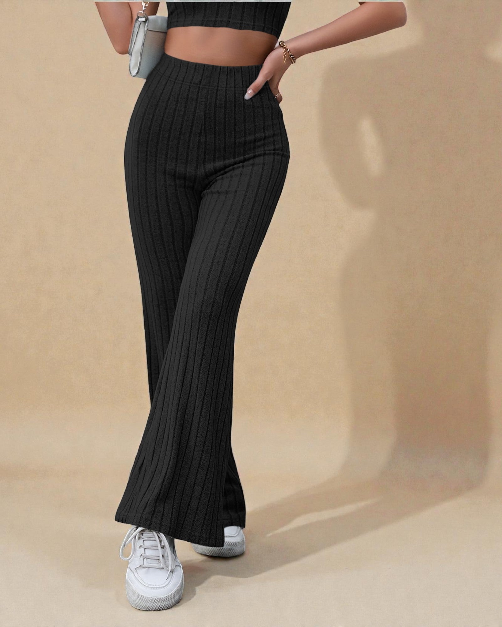 Person wearing black ribbed pants and white sneakers on a beige background