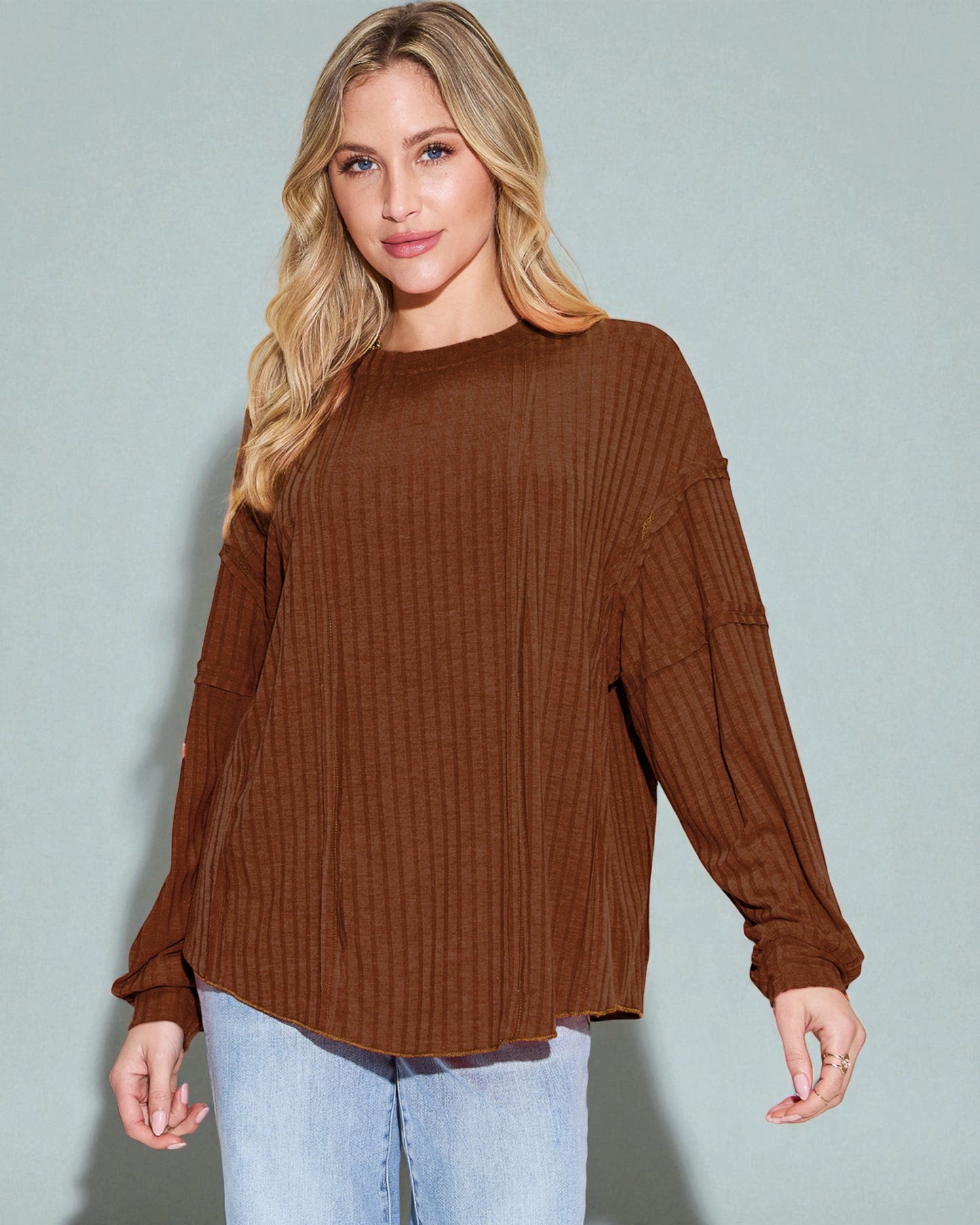 Woman wearing a brown ribbed sweater and light blue jeans against a gray background