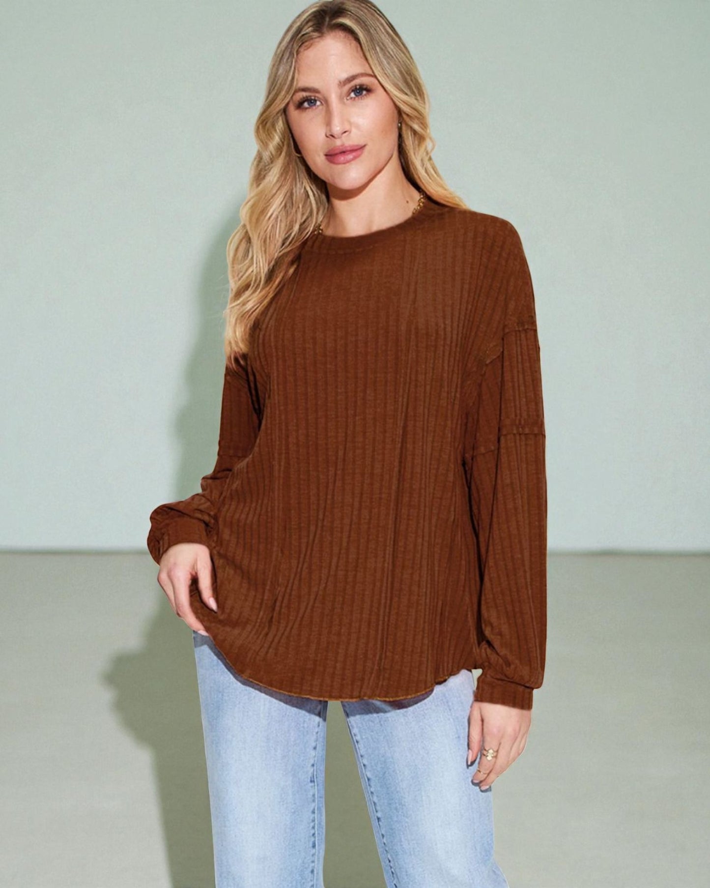 Woman wearing a brown ribbed sweater and light blue jeans against a plain background