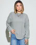 Woman wearing a gray ribbed sweater and blue jeans against a white background