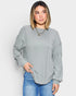 Woman wearing a light gray ribbed sweater and blue jeans on a white background