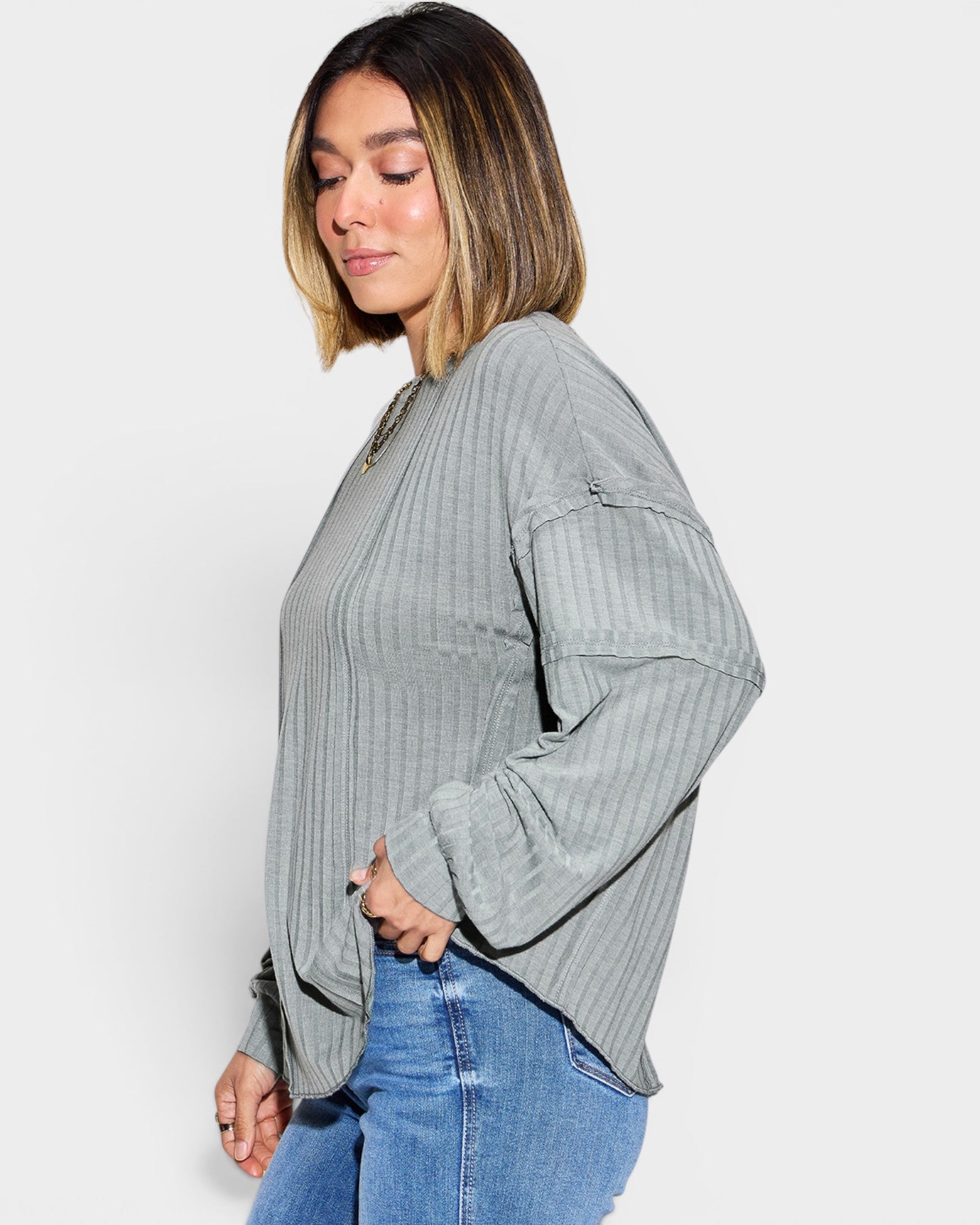 Woman wearing a gray ribbed sweater with black trim and blue jeans on a white background