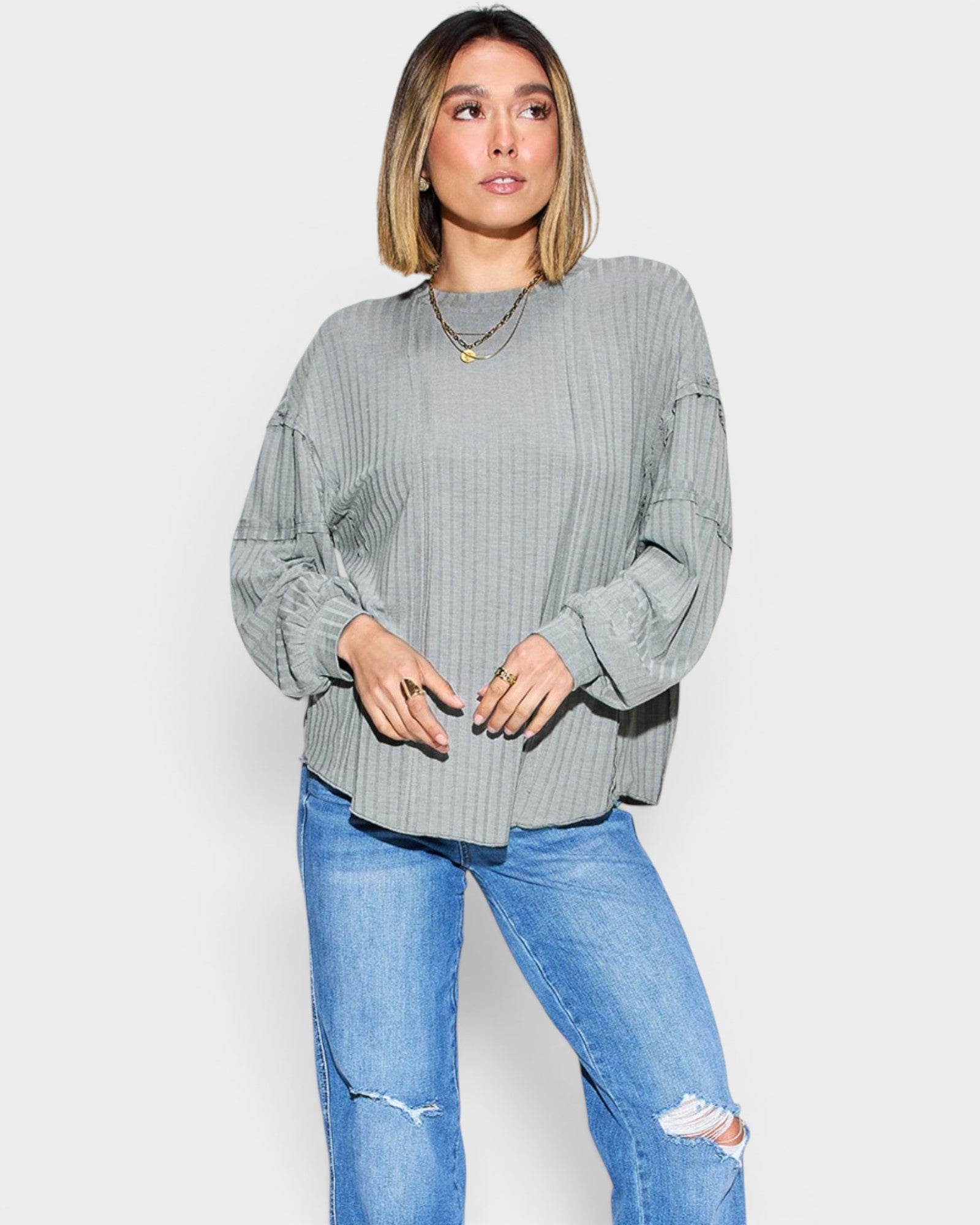 Woman wearing a gray ribbed sweater and blue jeans on a white background