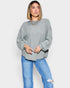 Woman wearing a gray ribbed sweater and blue jeans on a white background