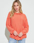 Woman wearing an orange textured sweater against a white background