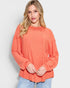 Woman wearing a coral ribbed sweater against a light background