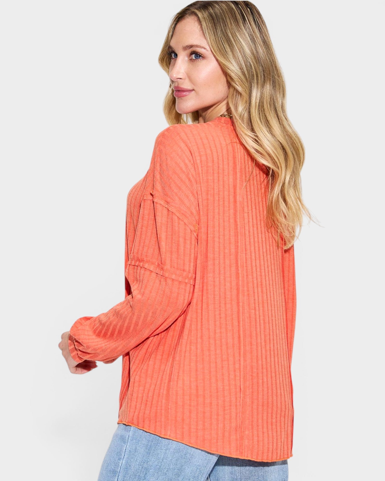 Woman wearing a coral ribbed sweater on a light gray background