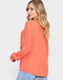 Woman wearing a coral ribbed sweater on a light gray background