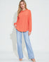 Woman wearing an orange sweater and light blue jeans on a white background