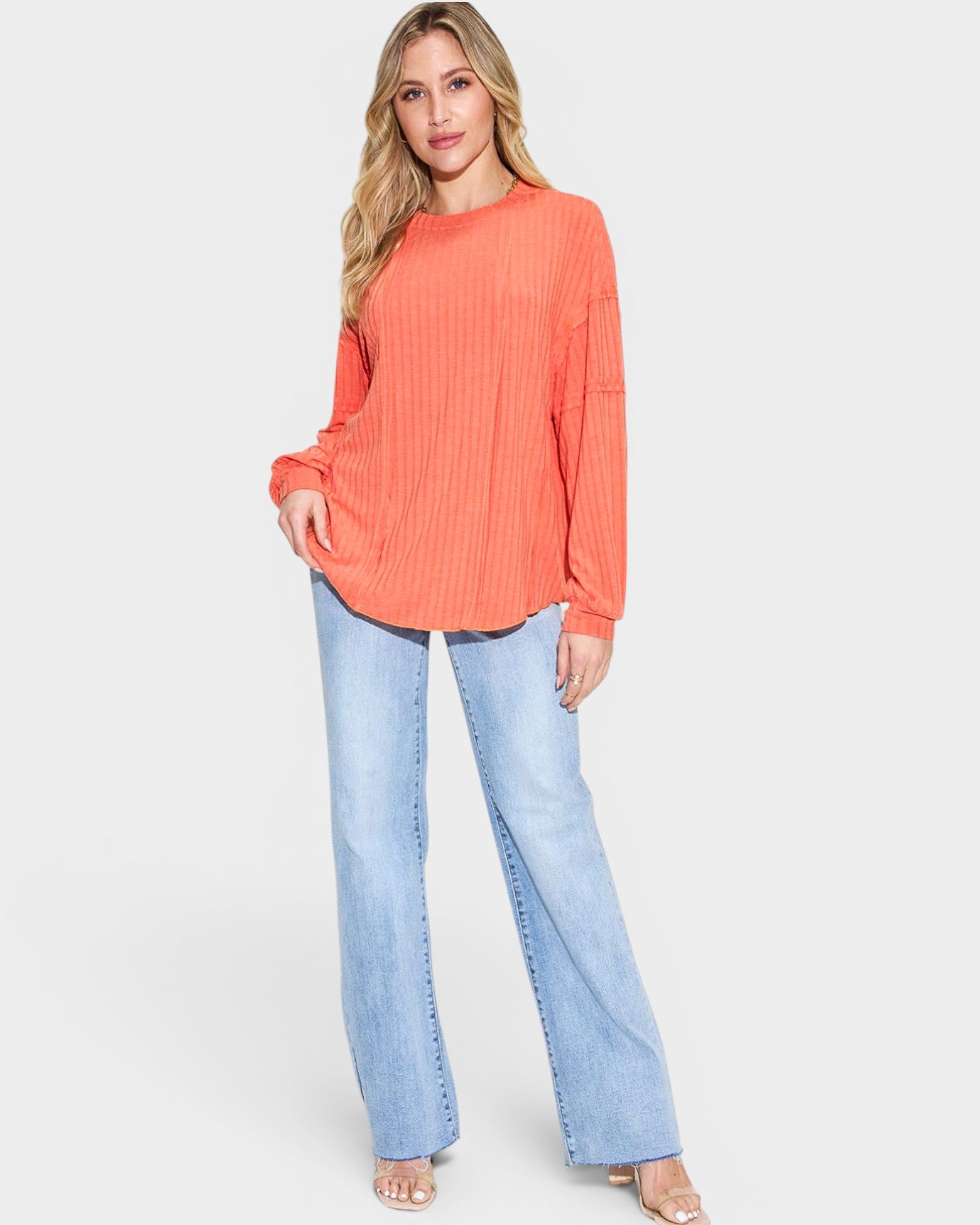 Woman wearing an orange sweater and light blue jeans on a white background
