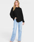Woman wearing a black sweater and light blue jeans on a white background