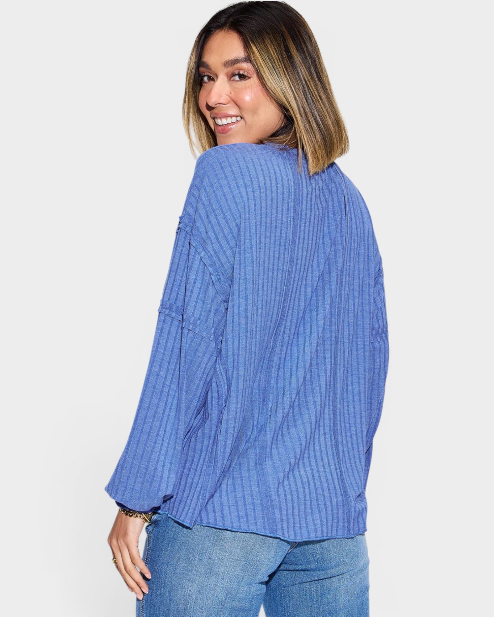 Woman wearing a blue ribbed sweater and jeans on a white background