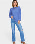Woman wearing a blue ribbed sweater and distressed jeans on a white background