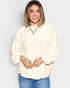 Woman wearing a light-colored blouse and blue jeans against a plain background