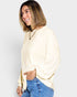 Woman wearing a beige sweater and blue jeans on a plain background