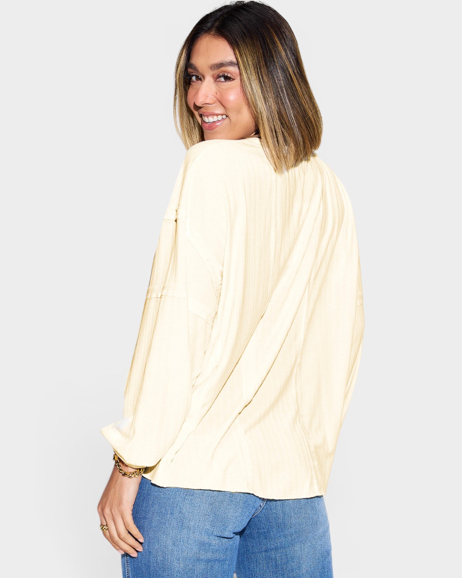 Woman wearing a light-colored blouse and blue jeans on a plain background