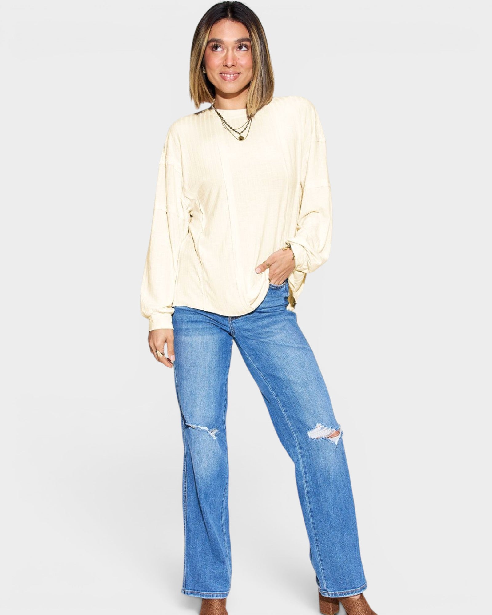 Woman wearing a cream blouse and blue jeans on a plain background