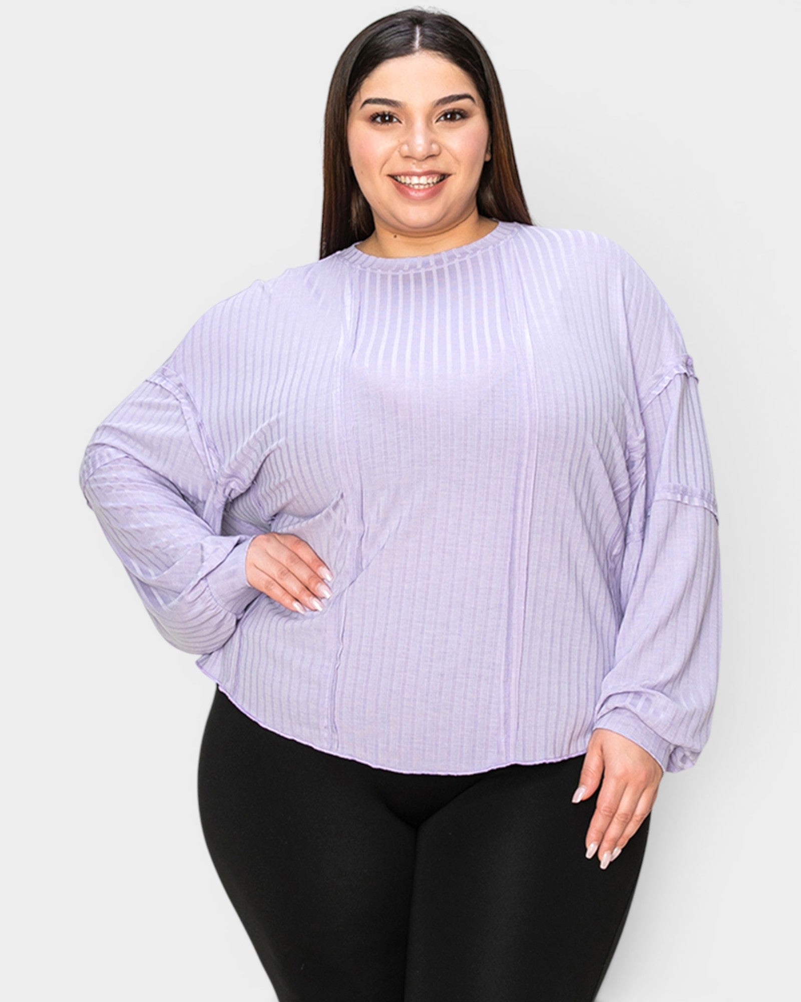 Woman wearing a light purple ribbed sweater and black leggings on a white background