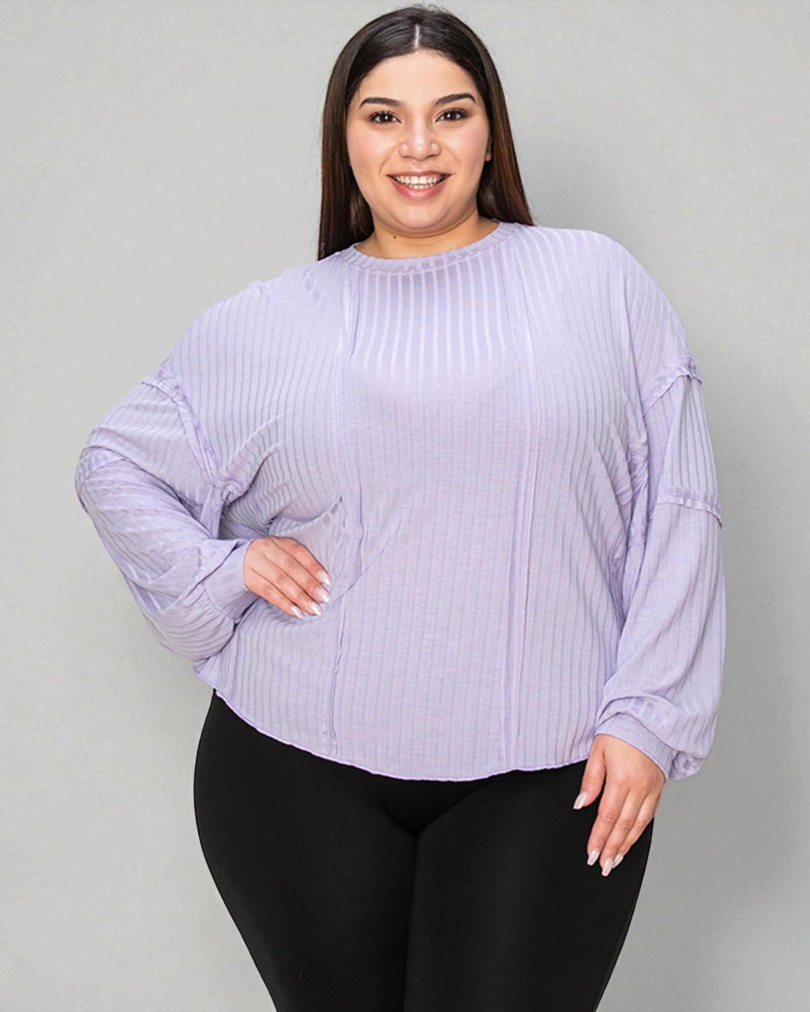 Woman wearing a light purple ribbed sweater and black pants against a gray background