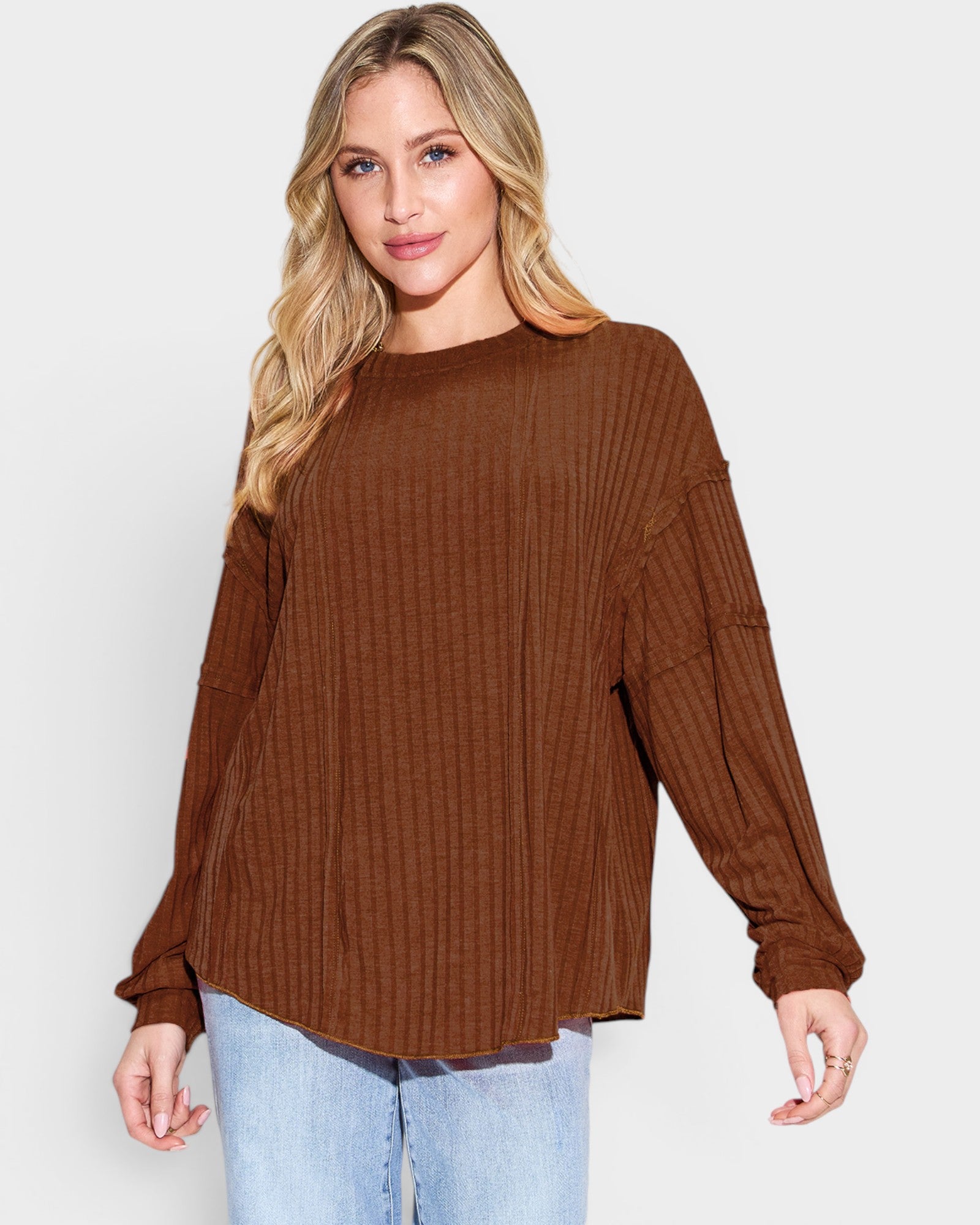 Woman wearing a brown ribbed sweater and light blue jeans on a white background