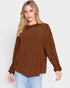 Woman wearing a brown ribbed sweater and light blue jeans on a white background