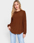Woman wearing a brown ribbed sweater and light blue jeans on a white background